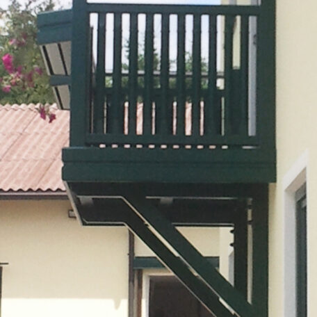 Kleiner Holzbalkon mit grünem Geländer an gelbem Haus, darüber ziegelgedecktes Dach. de HANSEL.kraus metalltechnik gmbh
