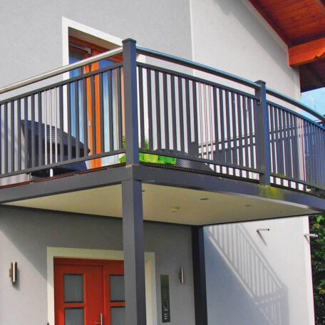 Moderner Balkon mit schwarzem Geländer an einem Einfamilienhaus, darunter rote Haustür, Tageslicht. HANSEL.kraus metalltechnik gmbh