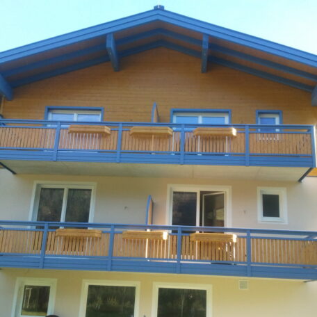 Zweistöckiges Haus mit blauen Holzbalkonen und großen Fenstern, Blick auf die Fassade. HANSEL.kraus metalltechnik gmbh