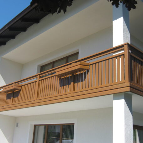 Moderner Holzbalkon an weißem Wohnhaus unter einem Dachvorsprung, Tageslicht, klarer Himmel. HANSEL.kraus metalltechnik gmbh
