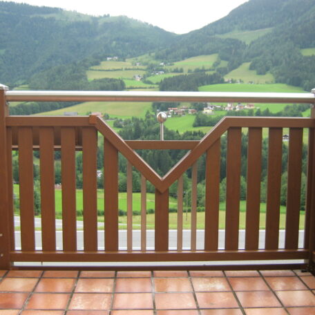 Holzgeländer auf Terrasse mit Blick auf grüne Wiesen und bewaldete Hügel im Hintergrund. HANSEL.kraus metalltechnik gmbh