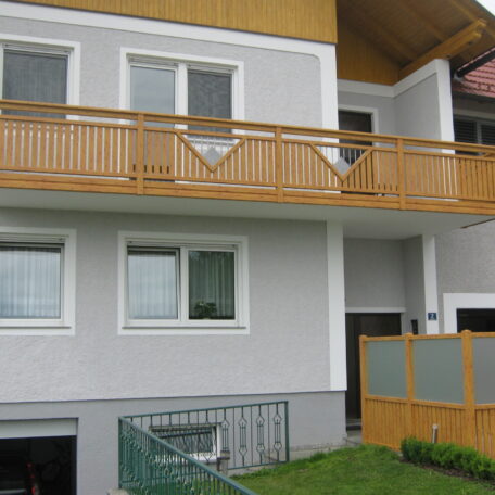 Zweistöckiges Wohnhaus mit Holzbalkon, weißen Fenstern und gepflegtem Vorgarten. de HANSEL.kraus metalltechnik gmbh