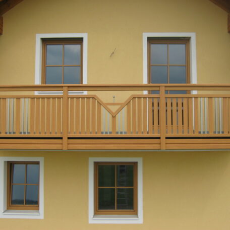 Zwei Fenster und ein Holzbalkon an gelber Hausfassade, Ansicht von vorne. HANSEL.kraus metalltechnik gmbh