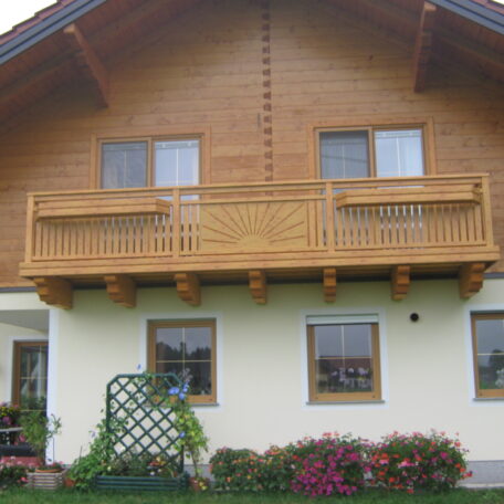 Zweistöckiges Holzhaus mit breitem Balkon und gepflegtem Garten, sonnige Außenansicht. HANSEL.kraus metalltechnik gmbh
