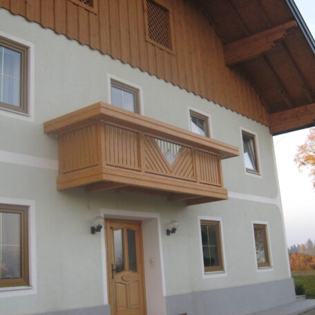 Fassade eines Einfamilienhauses mit Holzbalkon, mehreren Fenstern und Eingangstür. de HANSEL.kraus metalltechnik gmbh
