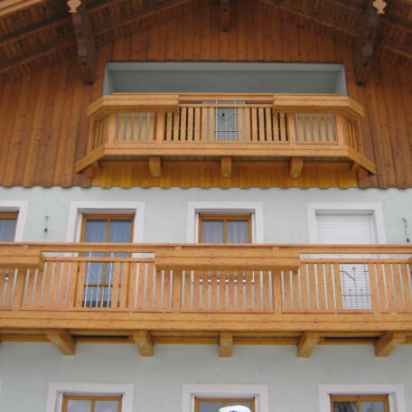 Zwei Holzbalkone an einer Fassade mit weißem Putz und oberen Holzelementen. HANSEL.kraus metalltechnik gmbh