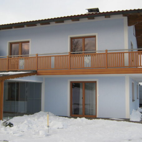 Zweistöckiges Haus mit Holz-Balkon und verschneitem Garten, Winterstimmung in ruhiger Wohngegend. HANSEL.kraus metalltechnik gmbh