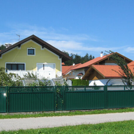 Zwei Einfamilienhäuser mit Garten und grünem Zaun an sonnigem Tag, blauer Himmel. HANSEL.kraus metalltechnik gmbh