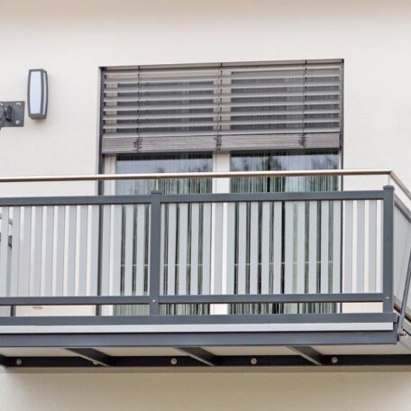 Moderner Balkon mit Metallgeländer, davor geschlossene Doppeltür und heruntergelassene Jalousien an einer Hausfassade. HANSEL.kraus metalltechnik gmbh