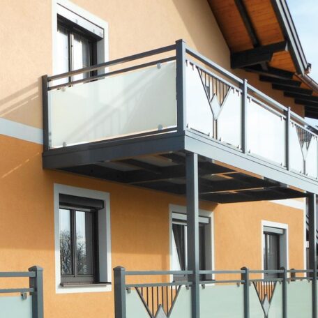 Moderner Balkon mit Glasgeländer an einem gelben Wohnhaus, Ansicht von außen. de HANSEL.kraus metalltechnik gmbh