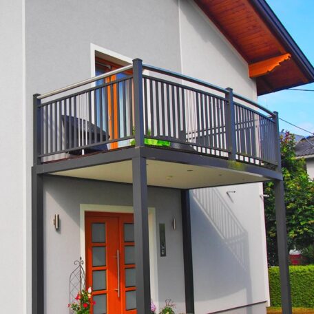 Moderner Balkon mit Metallgeländer an weißem Einfamilienhaus mit orangefarbener Haustür und Pflanze. HANSEL.kraus metalltechnik gmbh