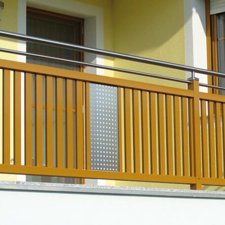 Gelbes Haus mit Holzbalkon und Tür, moderner Balkonbau, sonniger Außenbereich. HANSEL.kraus metalltechnik gmbh