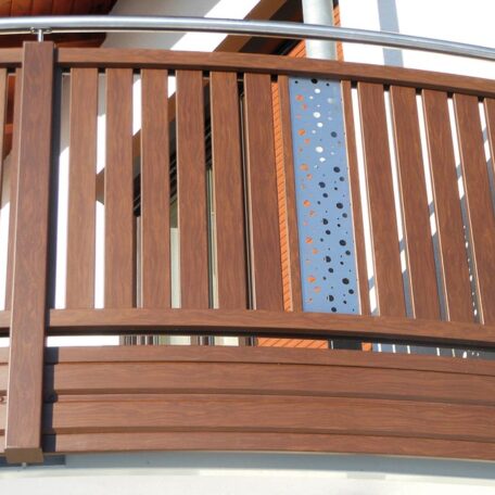Moderner Balkon mit braunem Holzgeländer und dekorativem Metall-Element in der Mitte. HANSEL.kraus metalltechnik gmbh