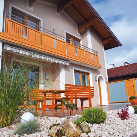 Modernes Einfamilienhaus mit Holzbalkon, Terrasse und gepflegtem Steingarten bei sonnigem Wetter. HANSEL.kraus metalltechnik gmbh
