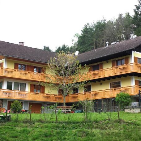 Mehrfamilienhaus mit Holz-Balkonen und grünem Garten am Waldrand, ländliche Umgebung. HANSEL.kraus metalltechnik gmbh