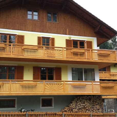 Traditionelles Alpenhaus mit Holzfassade, mehreren Balkonen und gestapeltem Brennholz im Erdgeschoss. de HANSEL.kraus metalltechnik gmbh