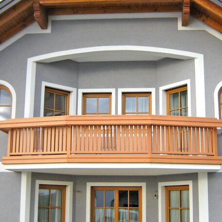 Holzbalkon an grauer Hausfassade mit weißen Fensterrahmen, geeignet für Imagefilm-Produktion in Freiburg. HANSEL.kraus metalltechnik gmbh