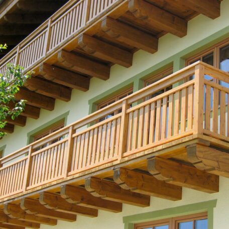 Balkongeländer aus Holz an einem traditionellen Haus, Sonnenschein und grüne Außenwand. HANSEL.kraus metalltechnik gmbh