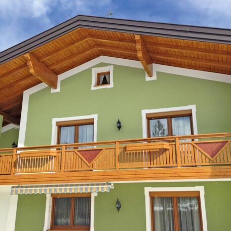 Haus mit grün verputzter Fassade, Holz-Balkon und Satteldach vor blauem Himmel. de HANSEL.kraus metalltechnik gmbh