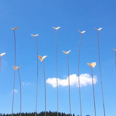 Kunstinstallation mit goldenen Vögeln auf Stäben vor blauem Himmel und einer Wolke. HANSEL.kraus metalltechnik gmbh