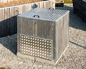 Quadratische Mülltonnenbox aus Holz und Metallgittern steht auf Kiesfläche draußen. HANSEL.kraus metalltechnik gmbh