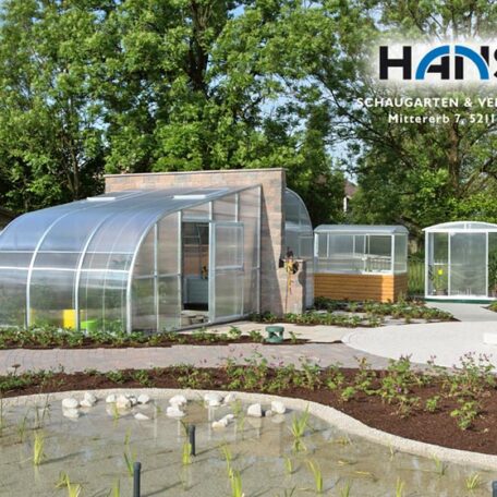 Mehrere moderne Gewächshäuser im Garten vor grünen Bäumen, Schild mit Hans-Logo sichtbar. HANSEL.kraus metalltechnik gmbh