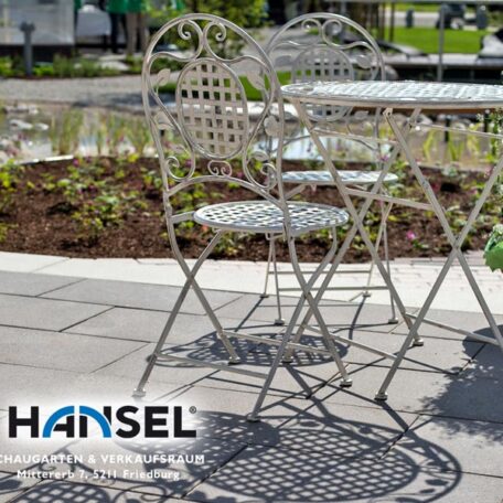 Gartenmöbel aus Metall stehen auf einer Terrasse im Grünen, Logo Hansel sichtbar. HANSEL.kraus metalltechnik gmbh