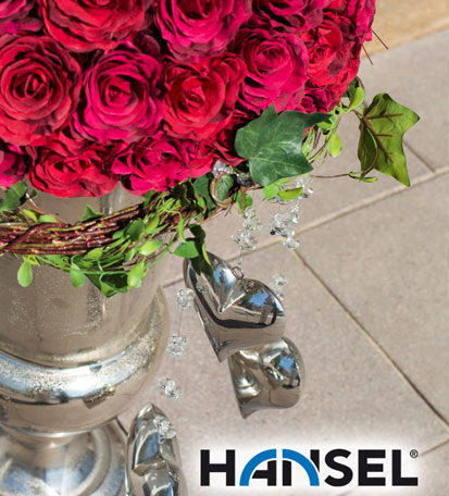 Rote Rosen in silberner Vase mit zwei silbernen Dekoherzen auf Steinboden. HANSEL.kraus metalltechnik gmbh