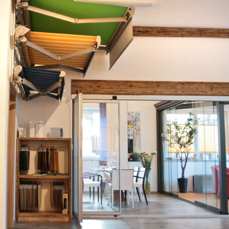 Ausgestellte Markisen in verschiedenen Farben und Stoffmuster im hellen Showroom mit Sitzbereich. HANSEL.kraus metalltechnik gmbh