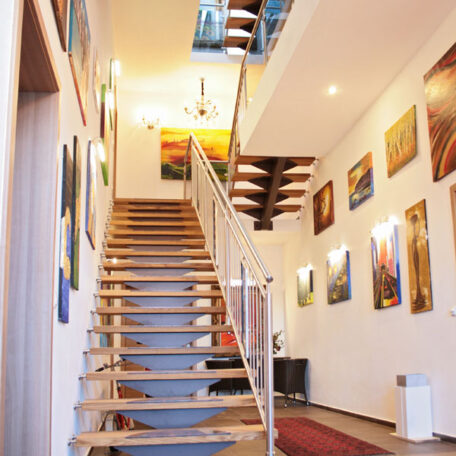Treppe mit Holzstufen, umgeben von modernen Gemälden an weißen Wänden in heller Galerie. de HANSEL.kraus metalltechnik gmbh