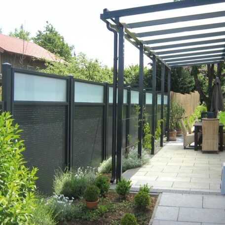 Moderner Sichtschutzzaun aus Glas und Metall neben einer Terrasse mit Pergola und Pflanzen. HANSEL.kraus metalltechnik gmbh