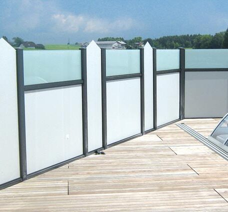 Sichtschutzwand aus Glas auf einer Holzterrasse vor blauem Himmel, ideal für Privatsphäre. HANSEL.kraus metalltechnik gmbh