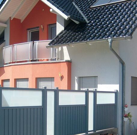 Modernes Einfamilienhaus mit Balkon, weiß-roter Fassade und grauem Sichtschutzzaun davor. HANSEL.kraus metalltechnik gmbh