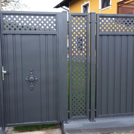 Metallzauntor mit Ornamenten und Sichtschutz neben einem gelben Haus im Gartenbereich. de HANSEL.kraus metalltechnik gmbh