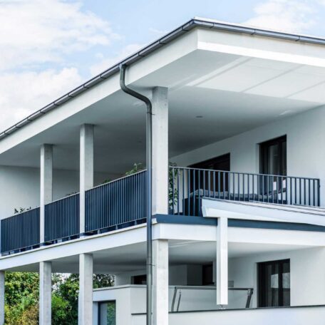 Modernes weißes Wohnhaus mit großer überdachter Terrasse und blauen Balkongeländern. HANSEL.kraus metalltechnik gmbh