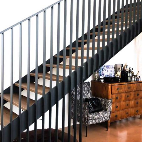 Moderne Treppe mit schwarzem Geländer, darunter Kommode und gemusterter Sessel in heller Wohnung. HANSEL.kraus metalltechnik gmbh