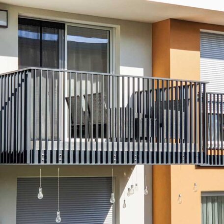 Moderner Balkon mit schwarzen Geländern an einer Hausfassade, zwei Stühle und ein Tisch. HANSEL.kraus metalltechnik gmbh