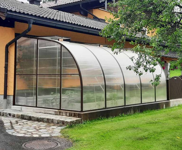 Gewölbtes Gewächshaus aus Glas steht im Garten neben einem traditionellen Haus auf Rasenfläche. HANSEL.kraus metalltechnik gmbh