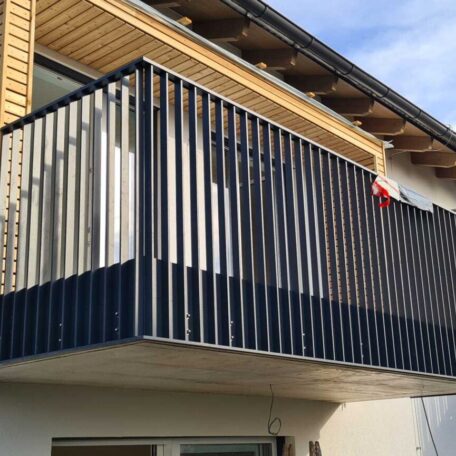 Moderner Balkon mit senkrechter Metallverkleidung an einer Fassade, blauer Himmel im Hintergrund. HANSEL.kraus metalltechnik gmbh