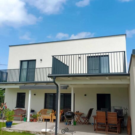 Modernes, zweistöckiges Einfamilienhaus mit großer Terrasse und Balkon, Gartenmöbel im Vordergrund. de HANSEL.kraus metalltechnik gmbh