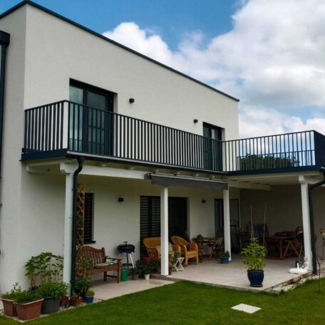 Modernes zweistöckiges Wohnhaus mit großem Balkon, Terrasse und gepflegtem Garten bei Sonnenschein. de HANSEL.kraus metalltechnik gmbh