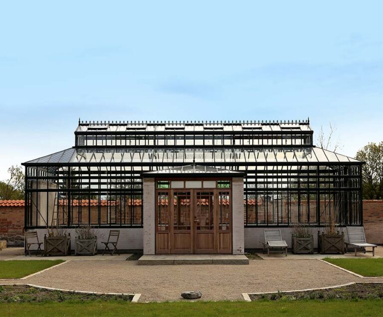 Historisches Gewächshaus mit Glaskonstruktion und Holztüren vor blauem Himmel. HANSEL.kraus metalltechnik gmbh