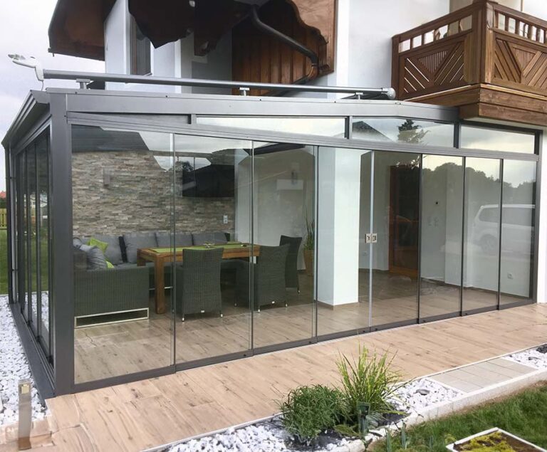Moderne Terrassenüberdachung aus Glas mit Sitzgruppe an einem Wohnhaus, Garten im Vordergrund. HANSEL.kraus metalltechnik gmbh