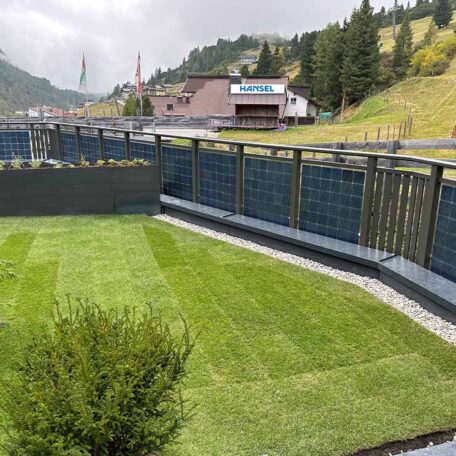 Frisch gemähter Rasen im Garten vor Zaun, Berge und Häuser im Hintergrund sichtbar. HANSEL.kraus metalltechnik gmbh