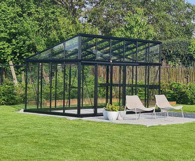 Modernes Glas-Gartenhaus mit zwei Liegestühlen auf einer Terrasse, umgeben von grünem Rasen und Bäumen. HANSEL.kraus metalltechnik gmbh