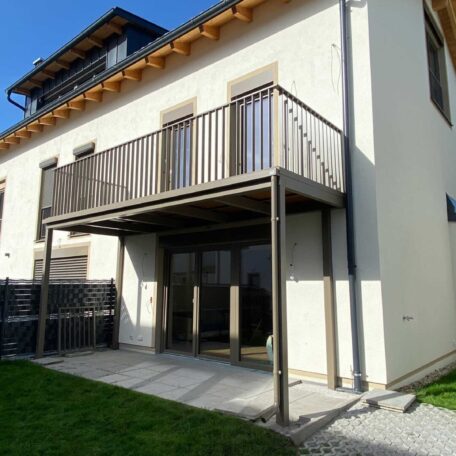 Modernes Wohnhaus mit großem Balkon, bodentiefen Fenstern und gepflegtem Garten an sonnigem Tag. HANSEL.kraus metalltechnik gmbh
