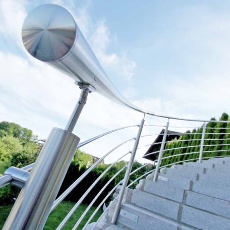 Modernes Edelstahlgeländer an einer geschwungenen Außentreppe mit grüner Bepflanzung im Hintergrund. HANSEL.kraus metalltechnik gmbh
