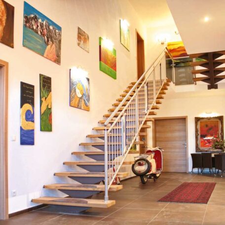 Offene Holztreppe in modernem Flur mit bunten Gemälden an weißer Wand. HANSEL.kraus metalltechnik gmbh