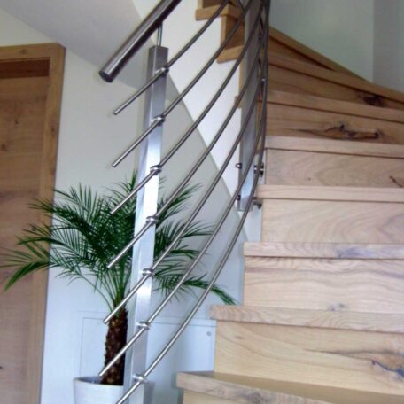 Hölzerne Treppe mit modernem Edelstahlgeländer, grüne Zimmerpflanze im Hintergrund. HANSEL.kraus metalltechnik gmbh