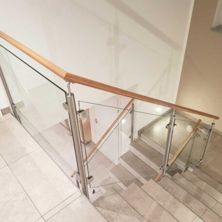 Moderne Treppe mit Glasgeländer und Holzhandlauf in einem hellen Innenraum. de HANSEL.kraus metalltechnik gmbh